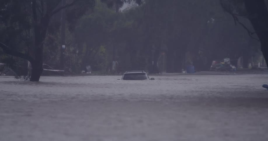 This footage shows a submerged car trapped in deep floodwaters during a heavy rainstorm the water level has risen high enough to almost completely cover the vehicle leaving only the roof and upper window line visible
