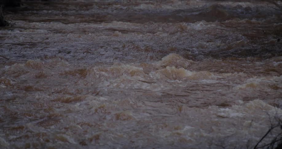 A tight closeup shot captures the turbulent surface of a muddy river its powerful current churning as it rushes past