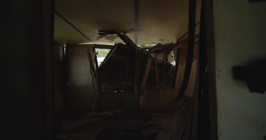 View through a doorway into a destroyed room with a collapsed ceiling and wooden debris scattered across the floor
