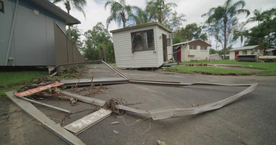 Broken wooden fence with signs and fallen vegetation in residential area after storm