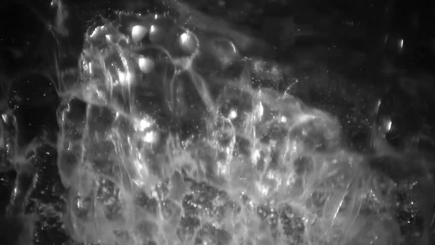 This video features a highcontrast blackandwhite shot of turbulent liquid or gas creating an abstract ethereal display of shifting highlightsthe fluid motion produces ghostly weblike patterns and rising bubbles that catch the light against a de