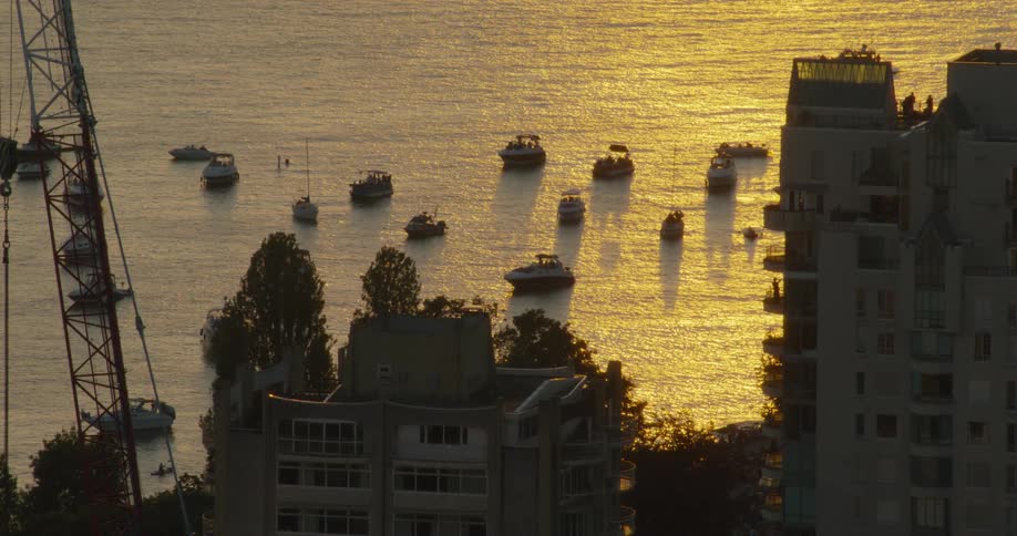 In a blackandwhite closeup shimmering liquid or bubbles rise and churn against a dark backgroundseveral small boats are anchored in a body of water that glows with a bright golden reflection from the sunset framed by the silhouettes of tall build