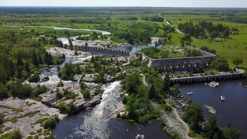 Water flowing through concrete dam surrounded by green grass and trees