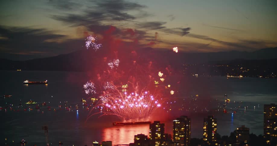 Event with fireworks at the sea in front of a metropolitan city next to the coast with mountains on the background outdoors during sunset time