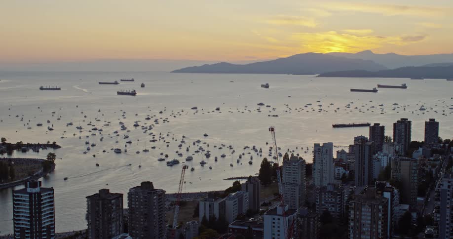 Aerial view of a coastal city at sunset with boats and cargo ships in the harbor