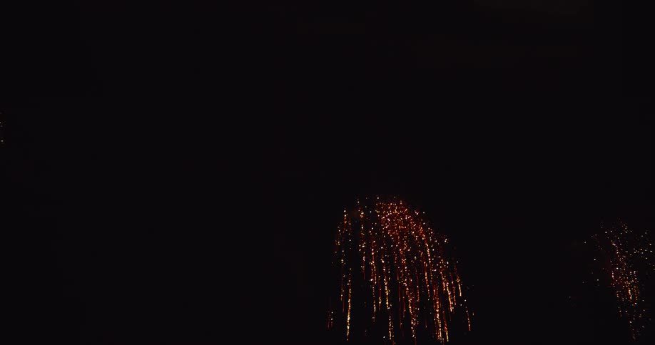 Golden fireworks explode against a black background with bright sparks spreading outwards and fading into the darkness