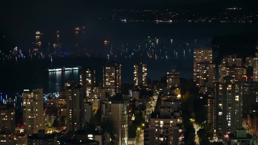 A city lit up at night with flashing lights in the harbor and many boats out