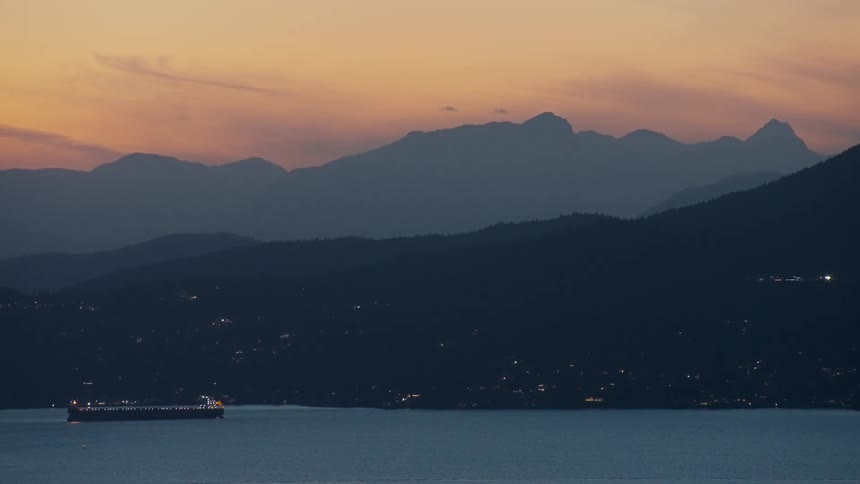 A cargo ship outdoors in the ocean at golden hour with the mountains in the background