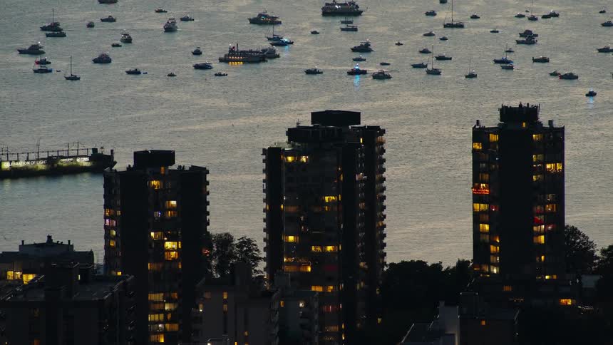 Several boats float in the water while lights shine from lit apartments in an apartment building