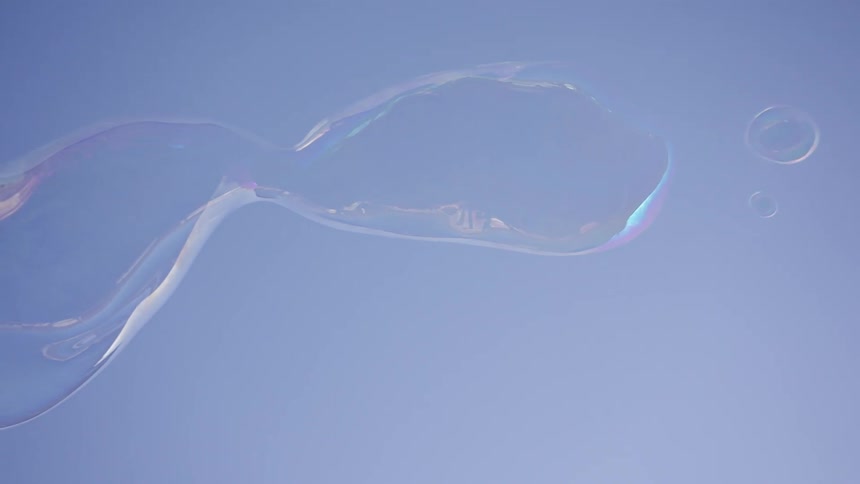 Large iridescent bubbles drift across a clear blue sky shimmering with rainbow colors as they stretch and warp in the airthe bubbles eventually break apart into smaller droplets and vanish leaving only the empty pale blue expanse
