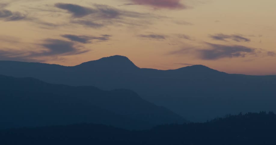 A mountain range stretches across the horizon at sunset glowing beneath an orange sky as the last light fades into a clear evening