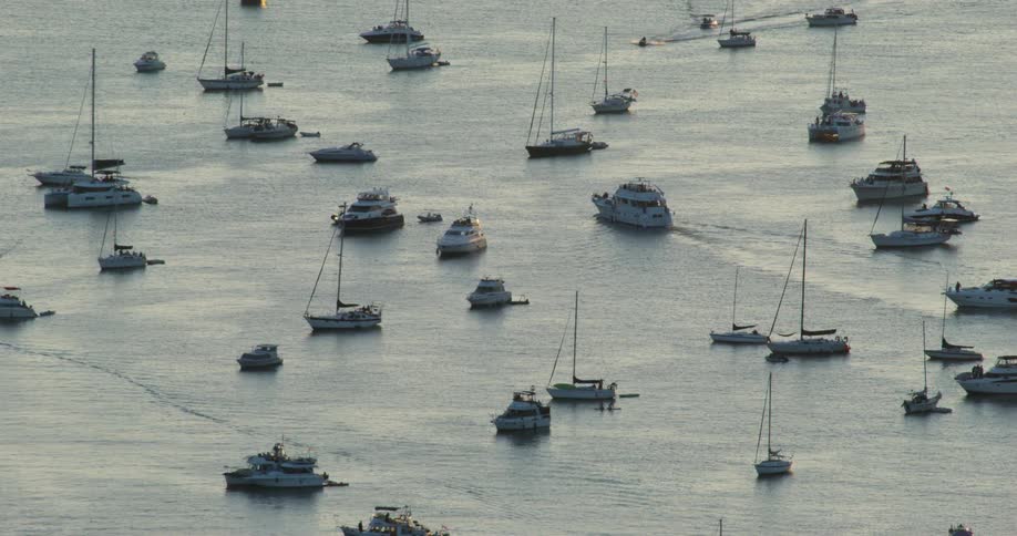 Various boats and yachts on calm bay waters at dusk with soft reflections