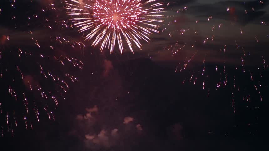 Colorful fireworks explode in the dark sky above silhouetted mountains creating bright sparks and drifting smoke