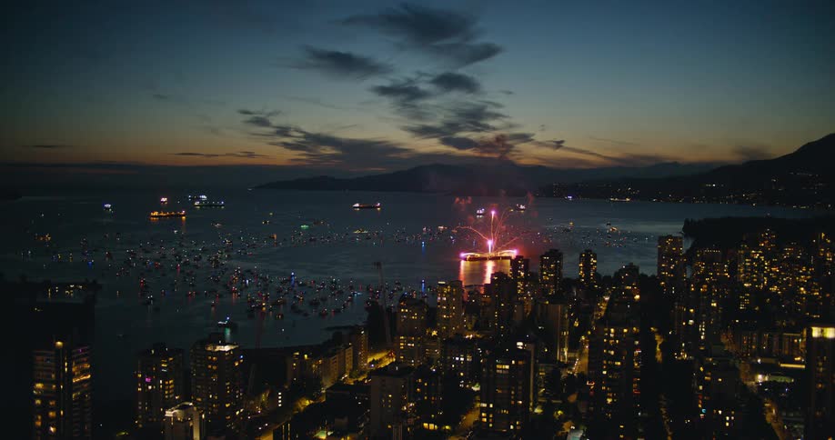 A city skyline at night its buildings illuminated by lights as fireworks brighten the sky above