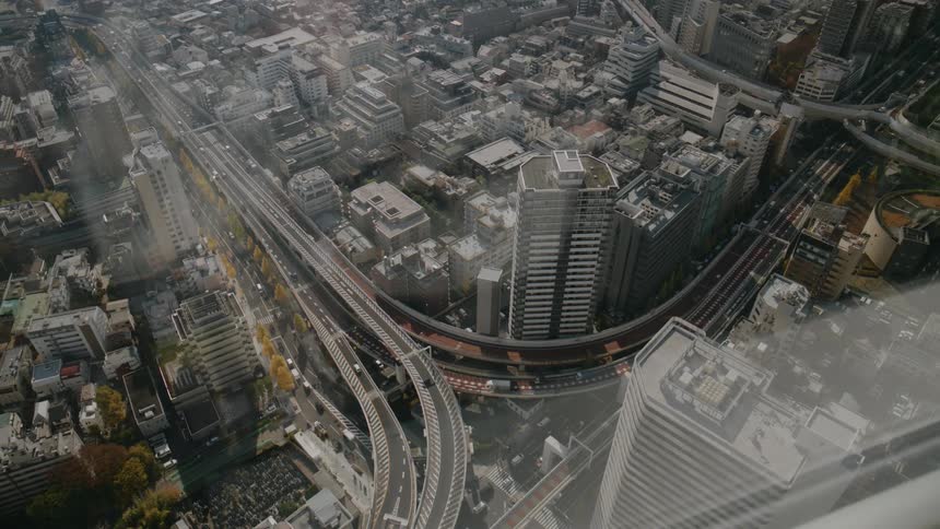 A highangle aerial view captures a complex multilevel highway interchange winding through a dense grid of skyscrapers and urban blocks as cars move along the curved expressway ramps between tall buildings