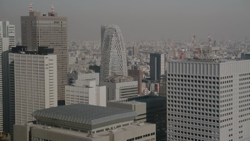A wide aerial shot overlooks a dense skyline featuring a modern skyscrapers surrounded by numerous gray office buildings under a hazy monochromatic sky during the day