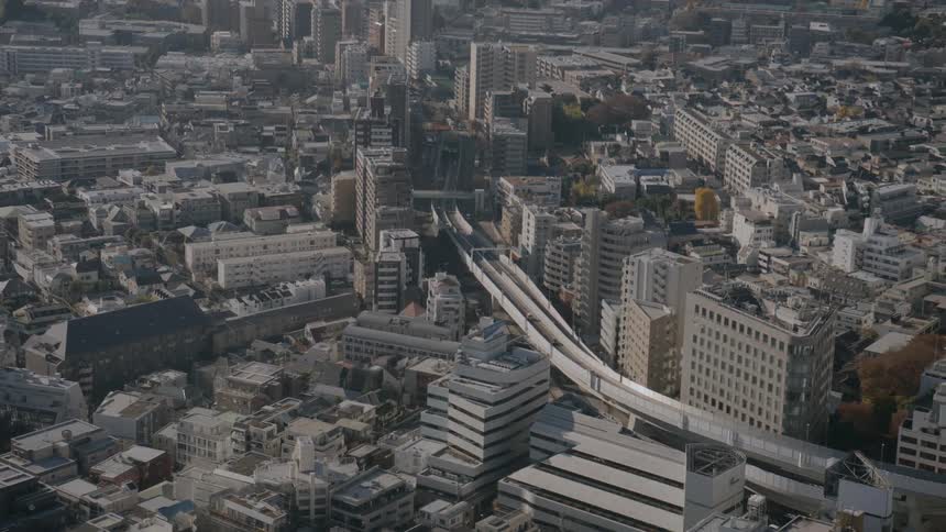 A highangle camera pans across a cityscape showing a complex network of residential blocks and commercial buildings centered around a winding elevated expressway and large modern skyscrapers under soft daylight