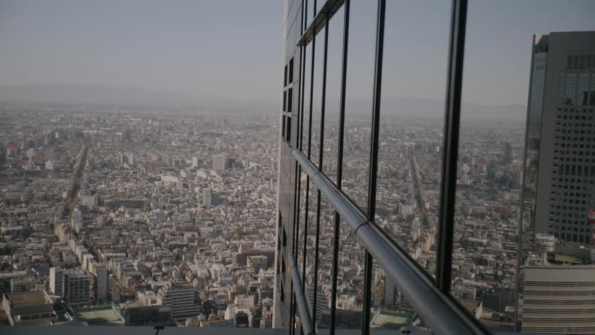 A city skyline viewed from a skyscraper at midday with sunlight illuminating the rooftops and stretching across the urban landscape below