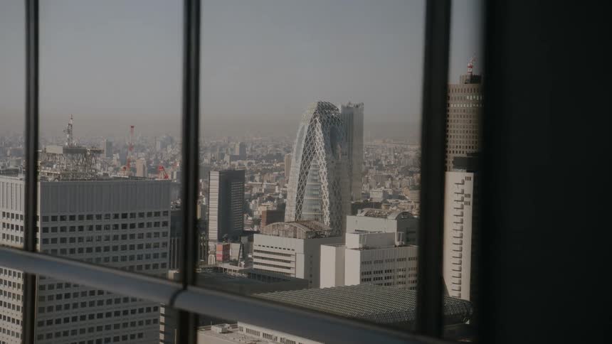 A city skyline seen through the glass windows of a skyscraper with rows of highrise buildings and towering skyscrapers stretching across the city under a bright sunny sky