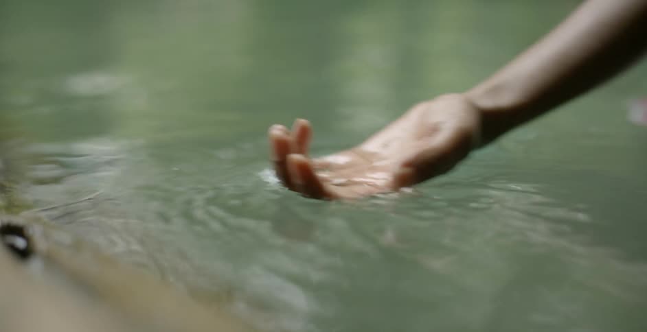 A person moves their hand palm up over water outside
