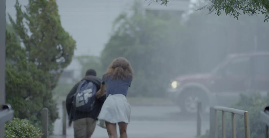 A woman gets out of the car in the rain to gather a waiting child