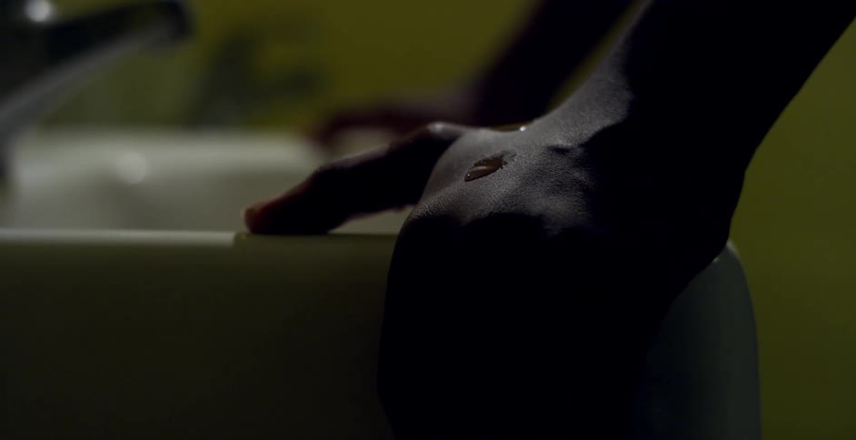 Water drops falling onto hand of person leaning against sink