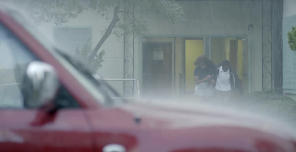 Man stands in a doorway and a woman runs in the rain to grab him