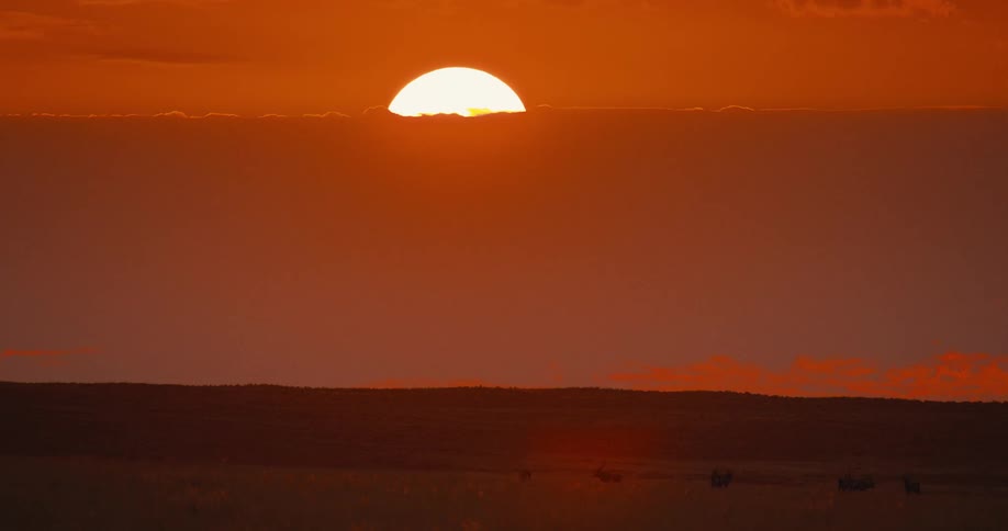 Sun glowing through a cloudy red sky over the landscape