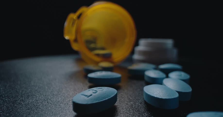 A pill container lies flipped over in a dark room its scattered pills spread across the surface beneath the faint moody lighting