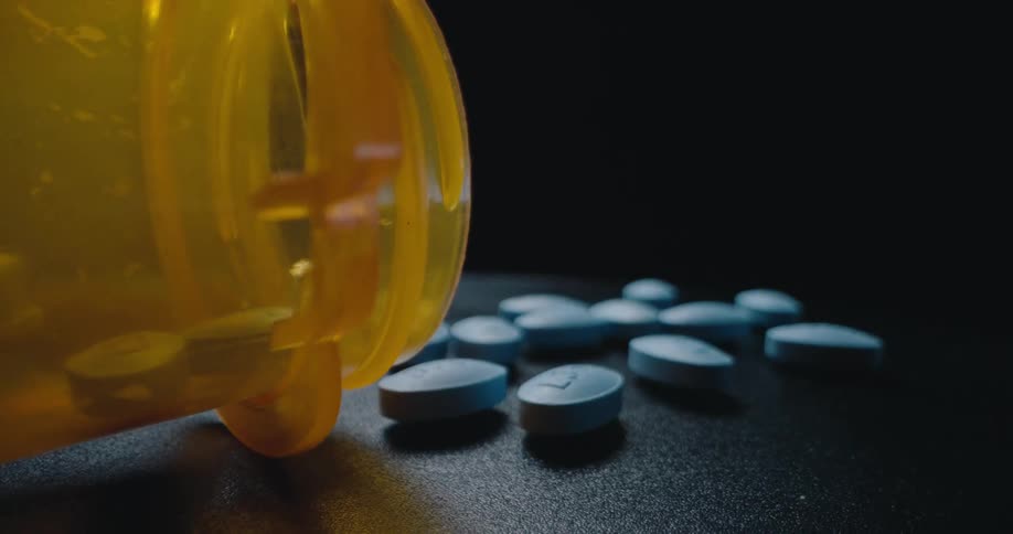 Blue pills next to a plastic bottle over a surface indoors