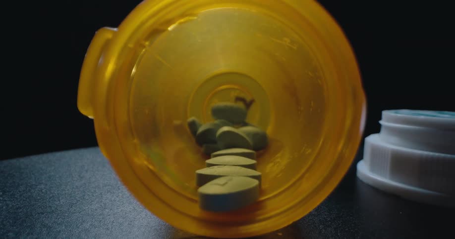 Open pill bottle spilling blue tablets onto a dark surface