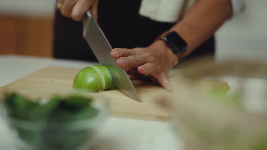 Adult male hands slicing a lime with a knife on a wooden cutting board over a counter indoors