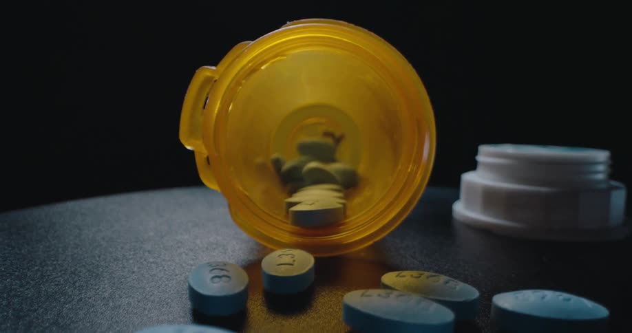 Blue pills scattered on a dark surface beside an open prescription bottle