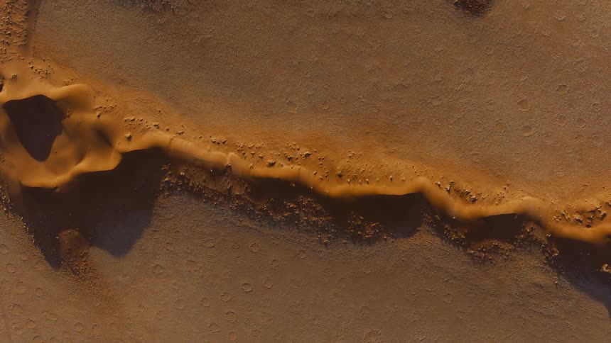 Wavy sand ridges cut across desert terrain with circular depressions