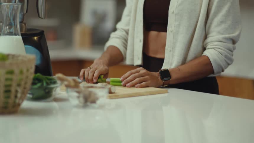 Woman slices celery on a cutting board to make a healthy smoothie in a modern kitchen
