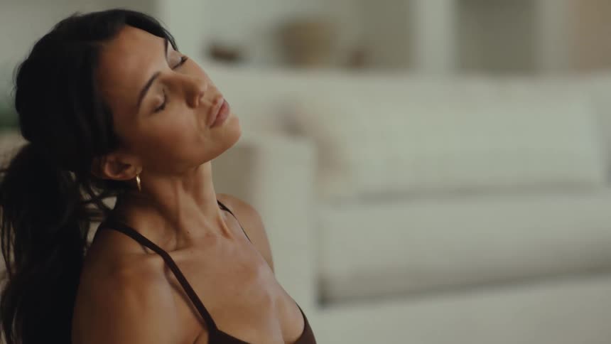 A woman performs a neck stretch in a brightly lit living room