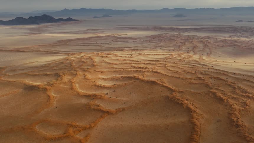Aerial view of a vast desert landscape with layered sand formations and distant mountains
