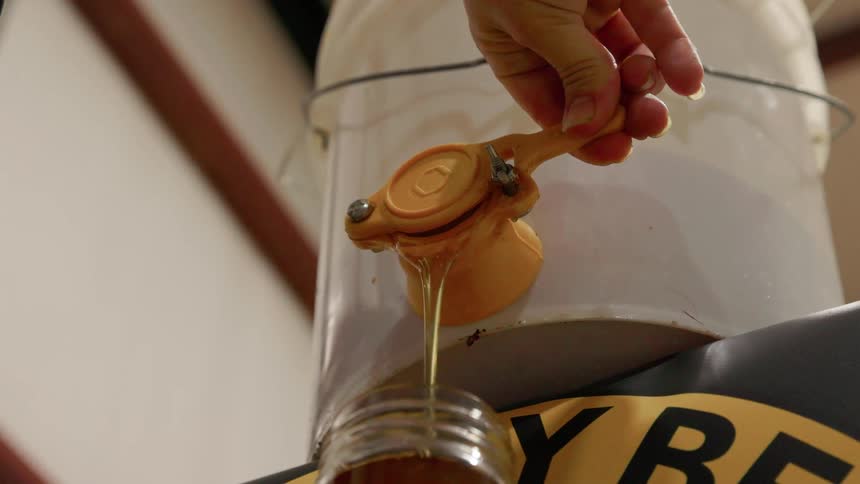 The farmer fills a jar with honey