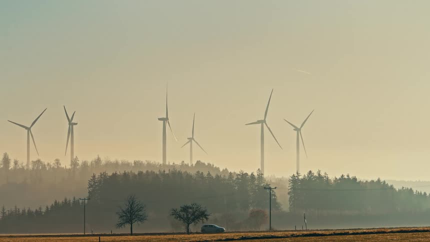 Turbines spinning on a wind farm as traffic moves by on the road