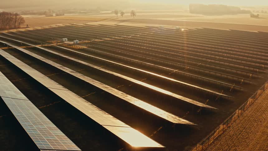 Aerial view of large solar panel fields stretching across rural farmland at sunrise