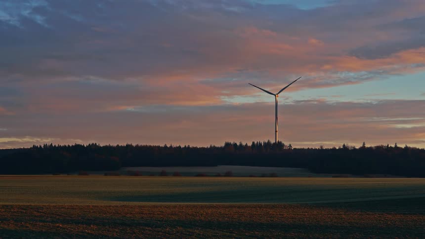 Wind turbine spins high above trees overlooking rural land