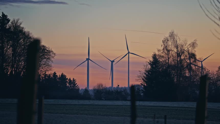 Wind turbines aligned on the horizon in a rural landscape at dusk