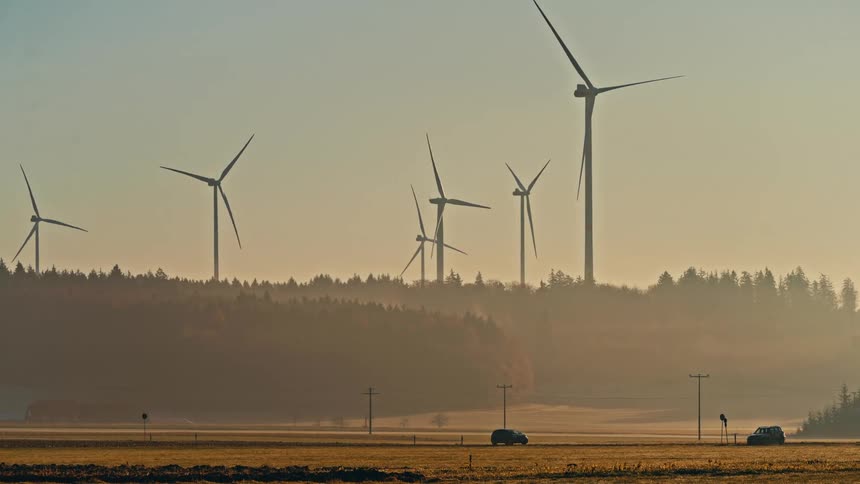 Powerful wind turbines rise on a misty forested ridge at dusk