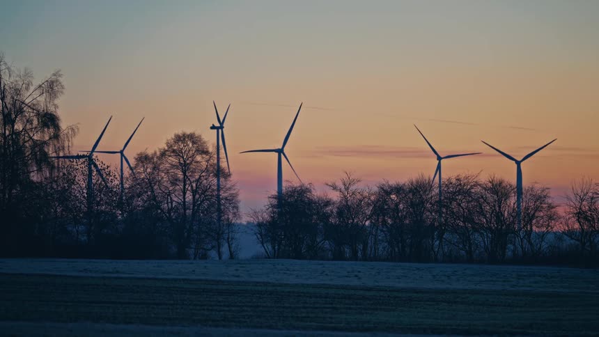 Turbines spin on a wind farm overlooking a valley