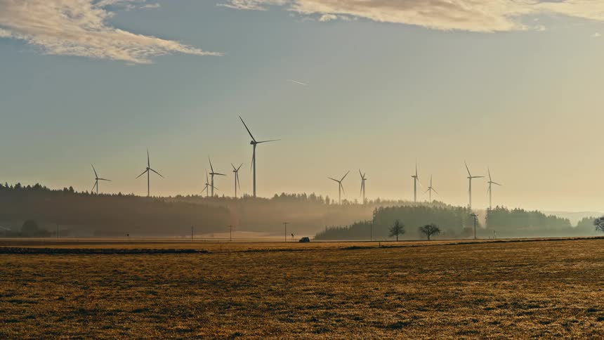 Turbines spin on a wind farm across the rural landscape