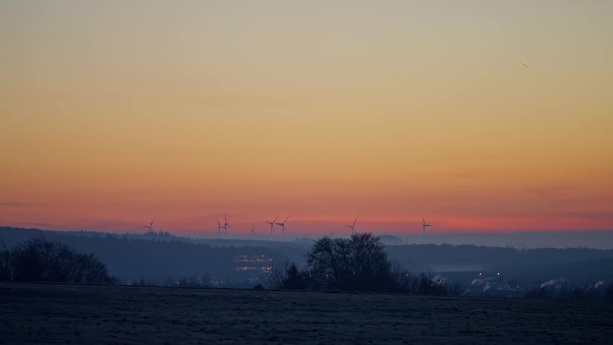 Wind turbines rise on horizon beneath orange sunset sky