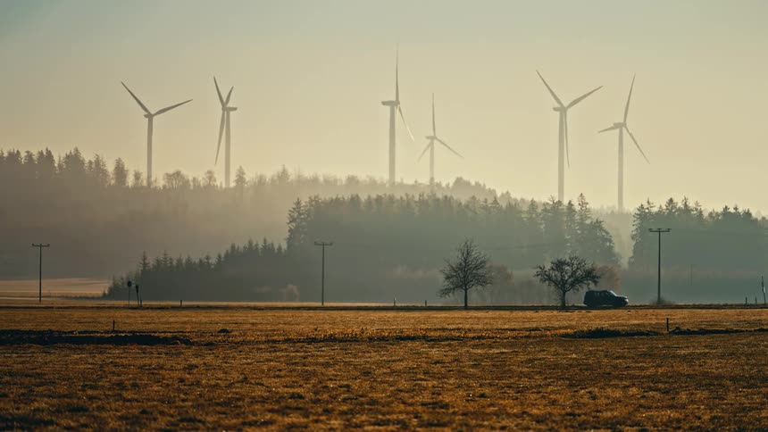 Powerful wind turbines rise above a rural field at dawn