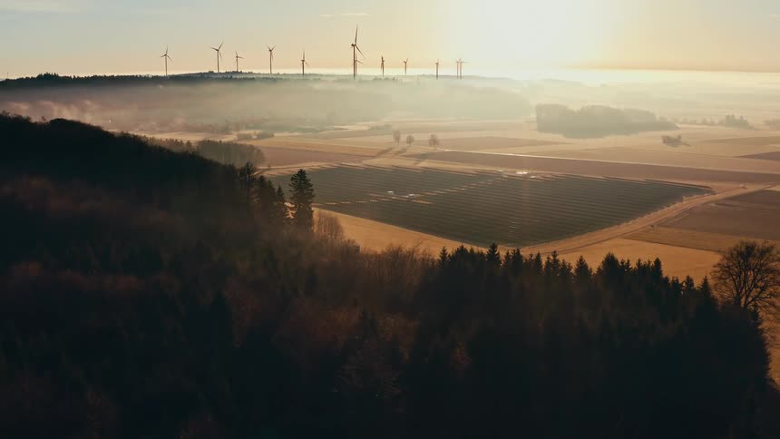 Aerial view of a wind turbines and solar panels in a foggy countryside at sunrise