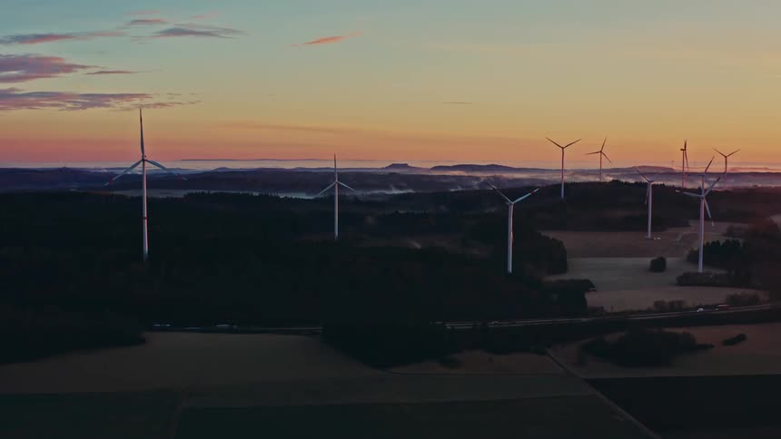 Turbines spinning on a wind farm along the coast as traffic moves on the road