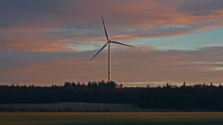 Wind turbine spins above the trees overlooking a rural field
